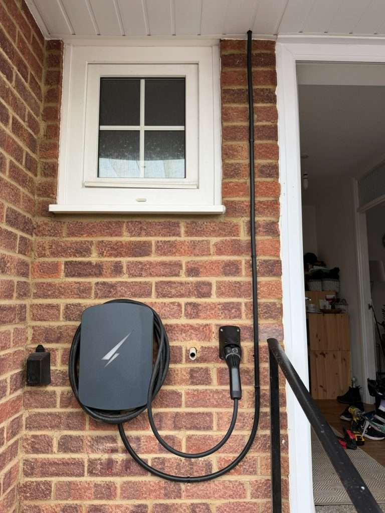 ev charger at house in maidenhead - db electrical services Home EV charger installation on brick wall, featuring charging unit and cable, showcasing discreet setup for residential properties in Marlow.