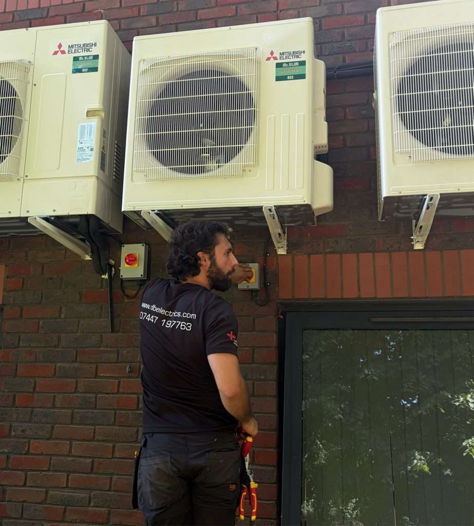 db electrical services air conditioning units Technician in black shirt repairing outdoor Mitsubishi Electric air conditioning units on a brick wall exterior.